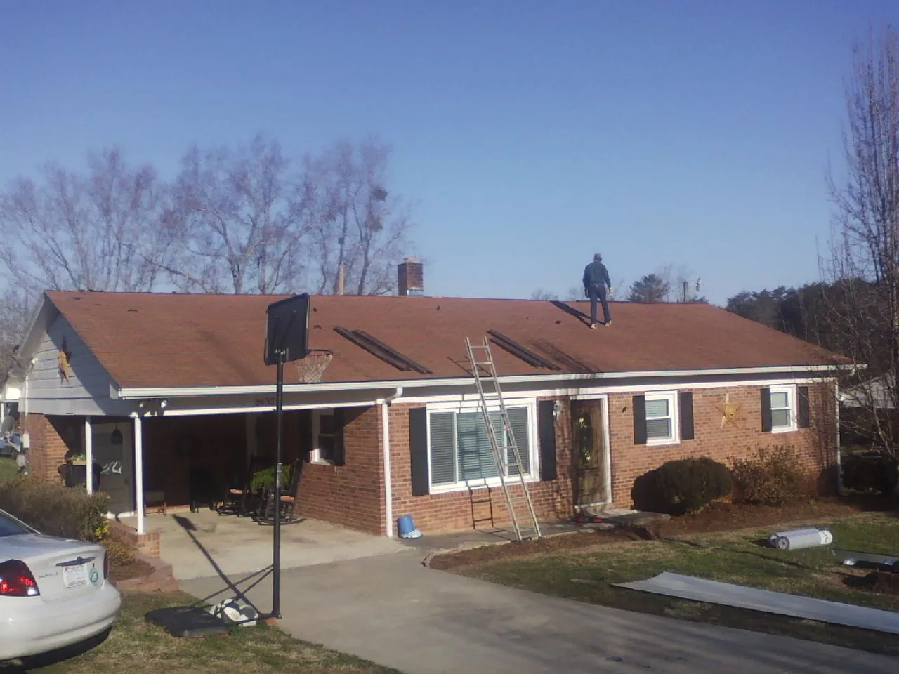Roofer stripping a shingle roof on a brick ranch before metal panels in Greenwood